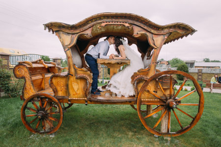 Happy sensual newlyweds kissing in old wooden carriage closeup.の写真素材