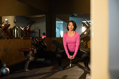Young lovely asian girl in pink sportwear doing exercise with dumbbells at the gym.