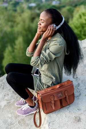 Moment of true peace and harmony. Pretty african american hipster young woman listening to music over blue cloudy sky background.の写真素材