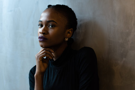 Close-up of thoughtful young black woman looking away with hand under the chin, gray background.の写真素材