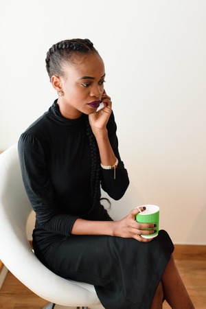 A mobile business woman in the office talking on her cell phone while holding disposable cup.の写真素材