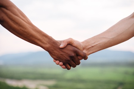 Close-up of mixed race couple holding hands on the green mountain background.の写真素材