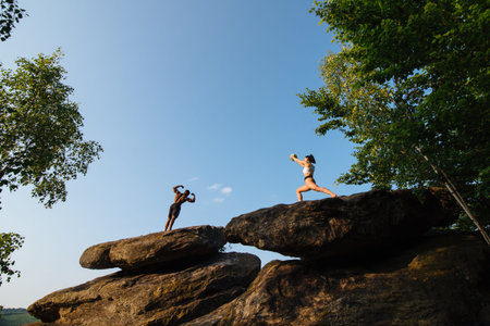 Mixed race couple of fitness trainers black bodybuilder and caucasian fit woman doing exercises together on the rocky peak. Sport health care conceptの写真素材
