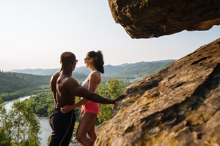 Fit muscular mixed race couple african american man bodybuilder and sexy brunette woman in sportswear embracing on the rocky mountains background.の写真素材