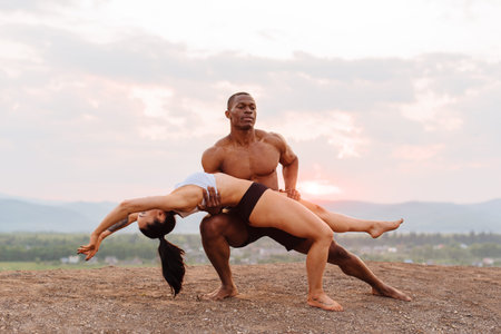 Mixed race gymnastic couple with perfect bodies in sportswear dancing on mountains landscape...