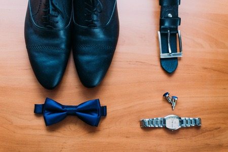 Close up of modern man accessories. Dark blue bowtie, leather shoes, belt, watch and cufflinks isolated on wood rustic background.の写真素材
