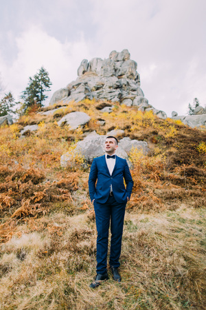 Portrait of handsome stylish groom in blue suit with a rocky natural landscape as background.の写真素材