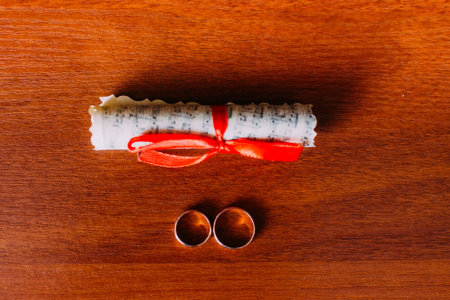Two wedding rings and fancy designed scrool with red strapping isolated on wooden rustic background.の写真素材