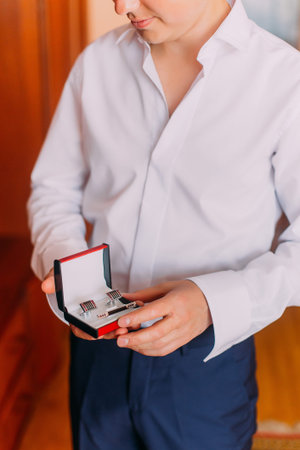 Attractive young man holding stylish red black box with cufflinks and tie clip while dressing in.