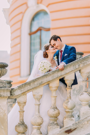 Beautiful young just married on stairs in park. Romantic antique palace at background.の写真素材