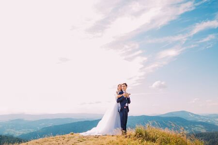 Portrait of beautiful newlyweds holding each other atop the hill with forest mountains as background.の写真素材