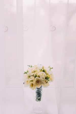 Beautiful bouquet of flowers in cut glass vase on windowsill. Bright window with white curtains at background.の写真素材