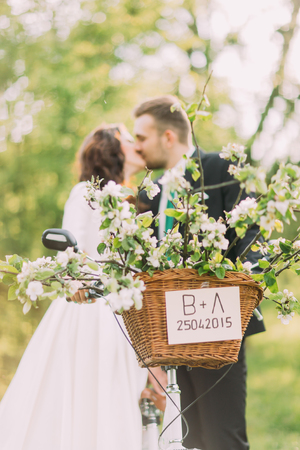 Sensual young newlywed couple kiss. Park outdoors. Focus on decorated bicycle basket.の写真素材