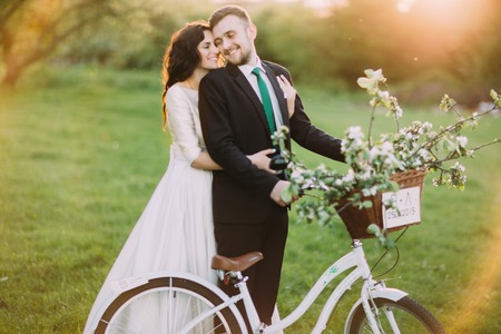 Romantic young couple posing in sunny park with decorated bicycle. Warm sun flares.の写真素材