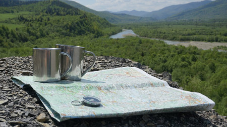 Travel accessories to the adventure in mountains: mug, conpass and map on the green nature...