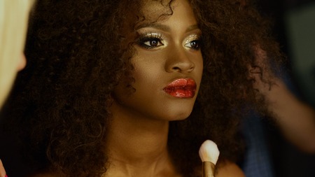 Surreal portrait of african american model with bright golden glitter makeup and glossy hairstyle preparing for shooting at the stylist.の写真素材