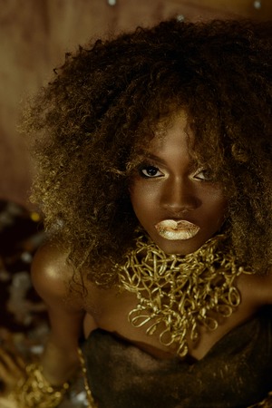Surreal portrait of sexy african american female model with glossy golden makeup posing to the camera on the studio background. Wild fashion concept.の写真素材