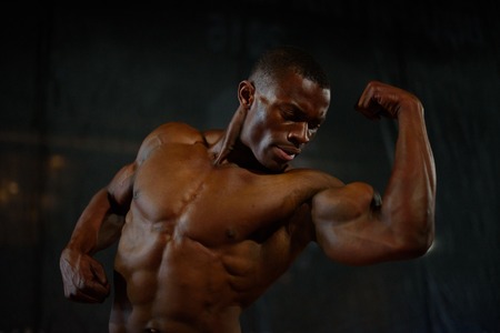 Close-up muscles of african american handsome body builder posing with naked torso on the black studio background.の写真素材