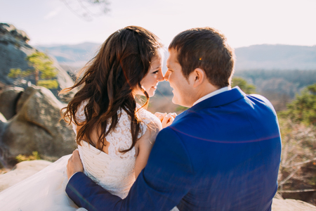 Romantic moment of newlywed couple holding each other in sunlight. Mountain landscape as backround. View from pair's back.の写真素材