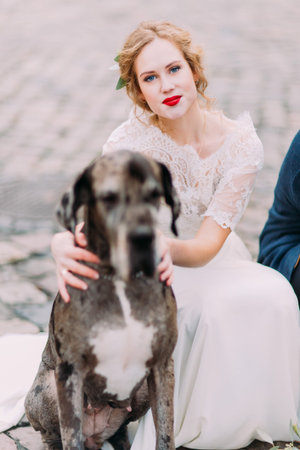 Beautiful blond bride with bright red lips holds her dog close up.の写真素材