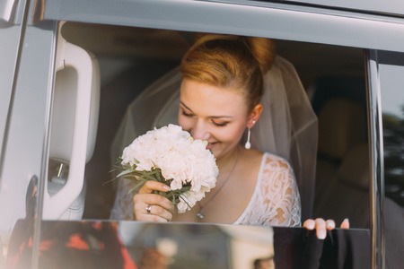 Happy beautiful blonde bride sniffs flowers in the car.の写真素材