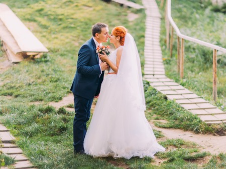 Beautiful redhair bride in a white dress with happy handsome groom kissing on background of rocky Carpathian mountains. Tustan fortress.の写真素材