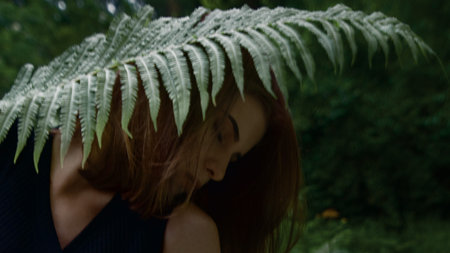 Beautiful young woman with closed eyes hiding behind exotic leaves.の写真素材