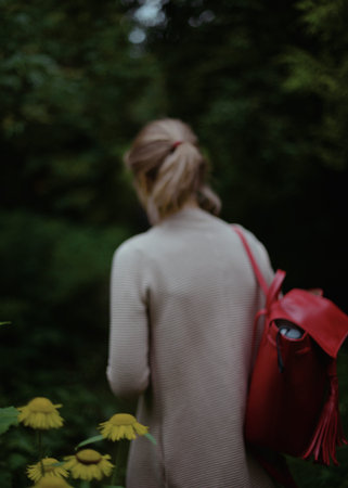 Blonde girl with the red backpack walking in the green park.の写真素材