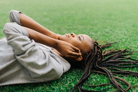Thoughtful young african american girl lying down on the grass listening to music with headphones.の写真素材