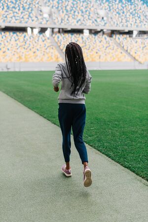 Fitness, sport, training, people and lifestyle concept - african american woman running on track outdoors from back.の写真素材