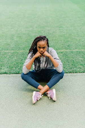 Bored african american young woman sitting at empty stadium with her chin resting on her hands and a...