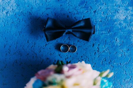 Still life with bow tie, wedding bouquet and pair of golden wedding rings on blue background.の写真素材
