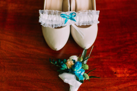 Close-up of cute bride's wedding accessories - boutonniere, shoes and garter on wooden background.の写真素材