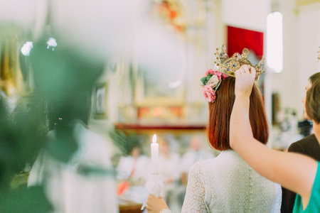 Bride holding a candle while bridesmaid hold a wedding crown over her, view from behind.の写真素材