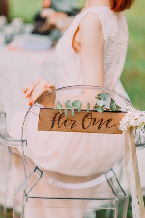 The bride in white dress sitting at served table with candles and bouquet, from the back. Chair with sign for her.の写真素材