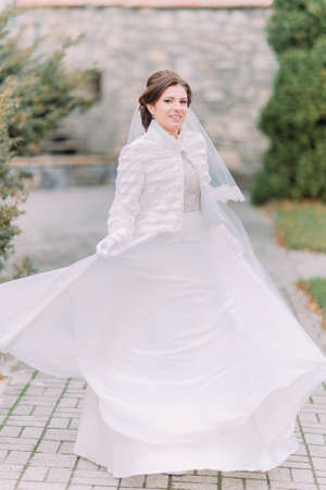 Beautiful elegant bride posing on green park paved road waving her gorgeous wedding dress.の写真素材