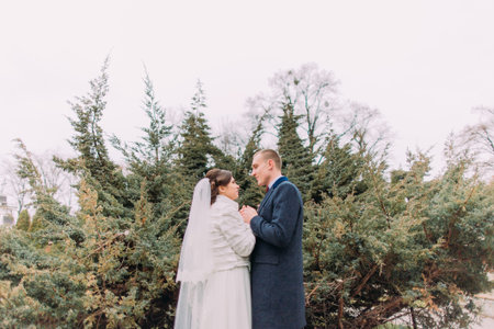 Happy newlywed couple holding hands and looking to each other at wedding walk on the beautiful green...