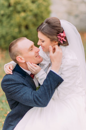 Happy newlywed couple outdoors. Elegant bride sitting on knees of her handsome new husband.