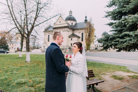 Panoramic view of beaytiful newlywed couple sensually holding hands in park near old baroque church.の写真素材