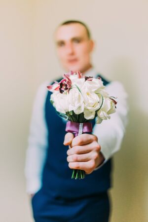 Stylish dressed man holding elegant bouquet indoor. Focus on flowers with blurred person image.の写真素材