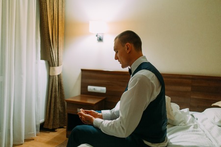 Young athletic man sitting in a hotel room on bed and looking to his hands.の写真素材