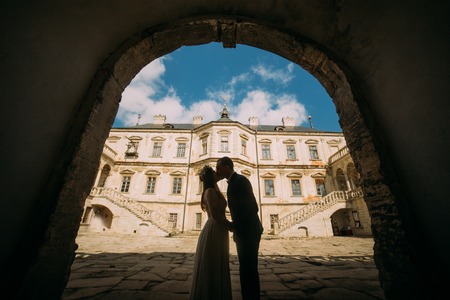 Passionate enloved couple share romantic at entrance arch of magnificent looking baroque palace shined by bright summer sun rays.の写真素材