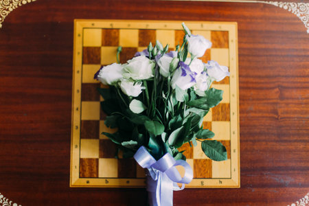 Bouquet of white roses lying on chessboard. Isolated at wooden table background.