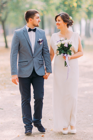 Happy newlywed couple posing outdoors when walking on park lane holding hands together.の写真素材