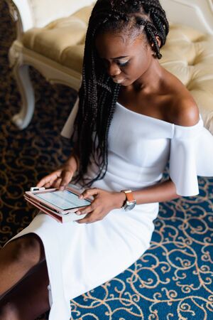 incredible beautiful black girl sitting on the floor chatting with friends in internet. Luxury interior with blue floor and classic furniture.の写真素材