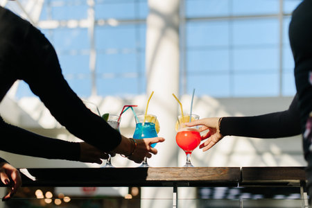 Three female hands taking alcohol cocktails. Sunlight. Golden bracelet.の写真素材