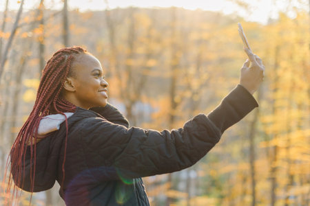 cute girl in autumn park making selfie. African woman smiling