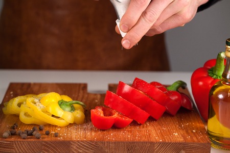Preparing vegetables using salt-shaker. Chef holding salt-shaker above sliced sweet pepperの写真素材