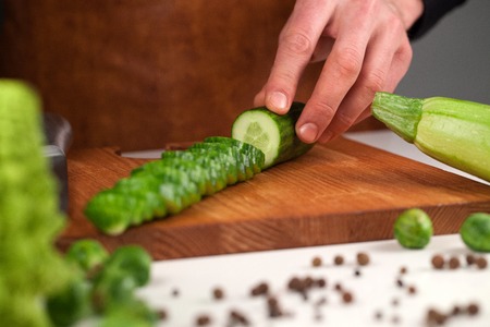 Sliced cucumber on a wooden cutting board neat set of different vegetables. Placed in front of chefの写真素材