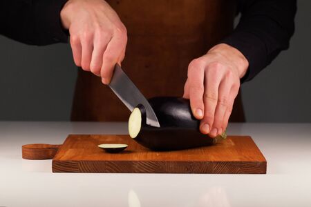 Man cutting big nice eggplant into slices on a wooden cutting boardの写真素材